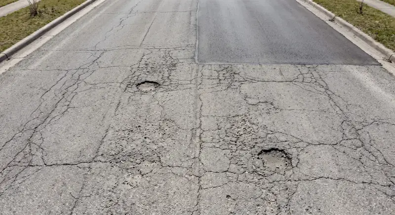 Cracked asphalt lane with two open potholes