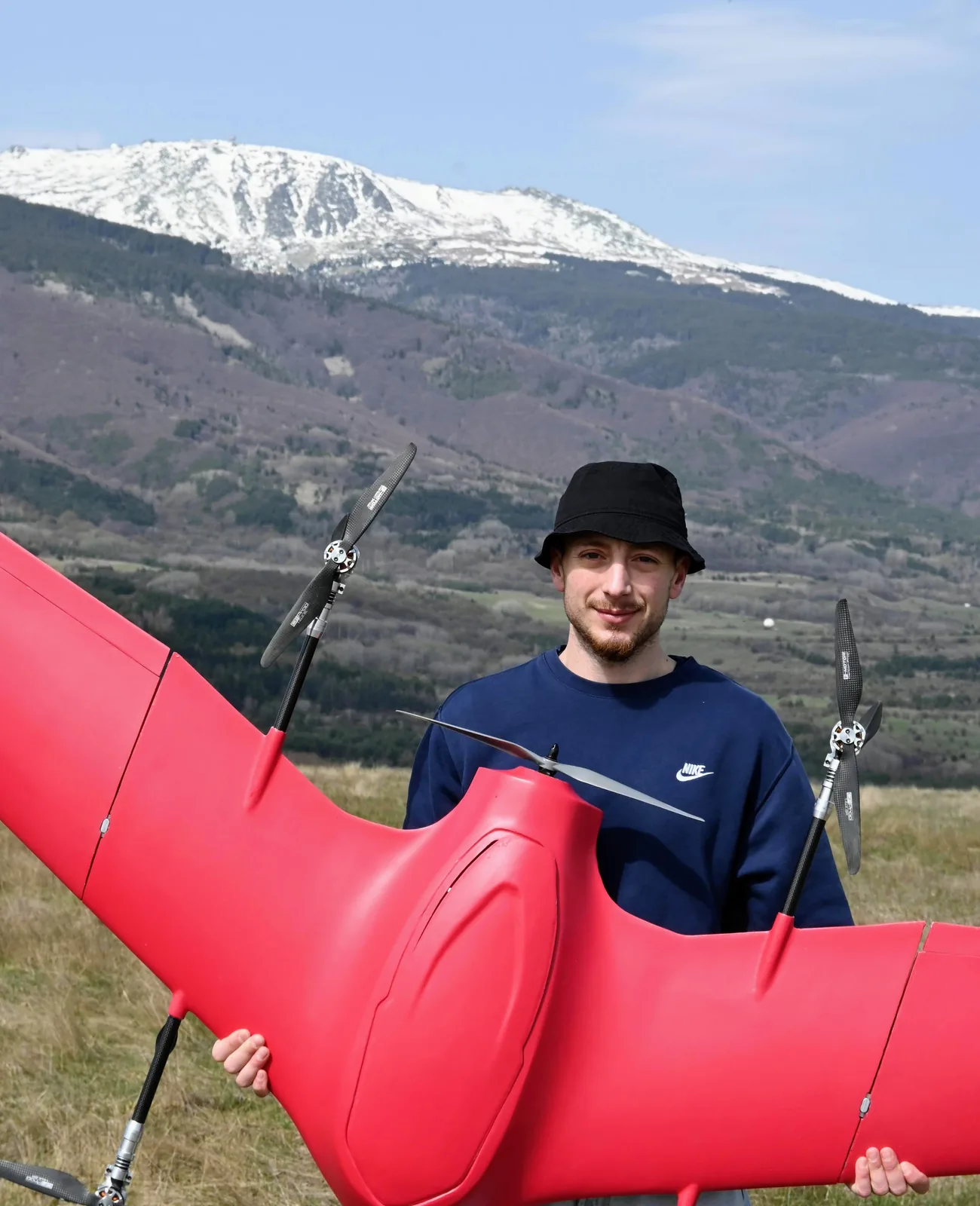 A crew member holding a fully assembled Nimbus across his body on a mountain meadow, snow-capped peak behind