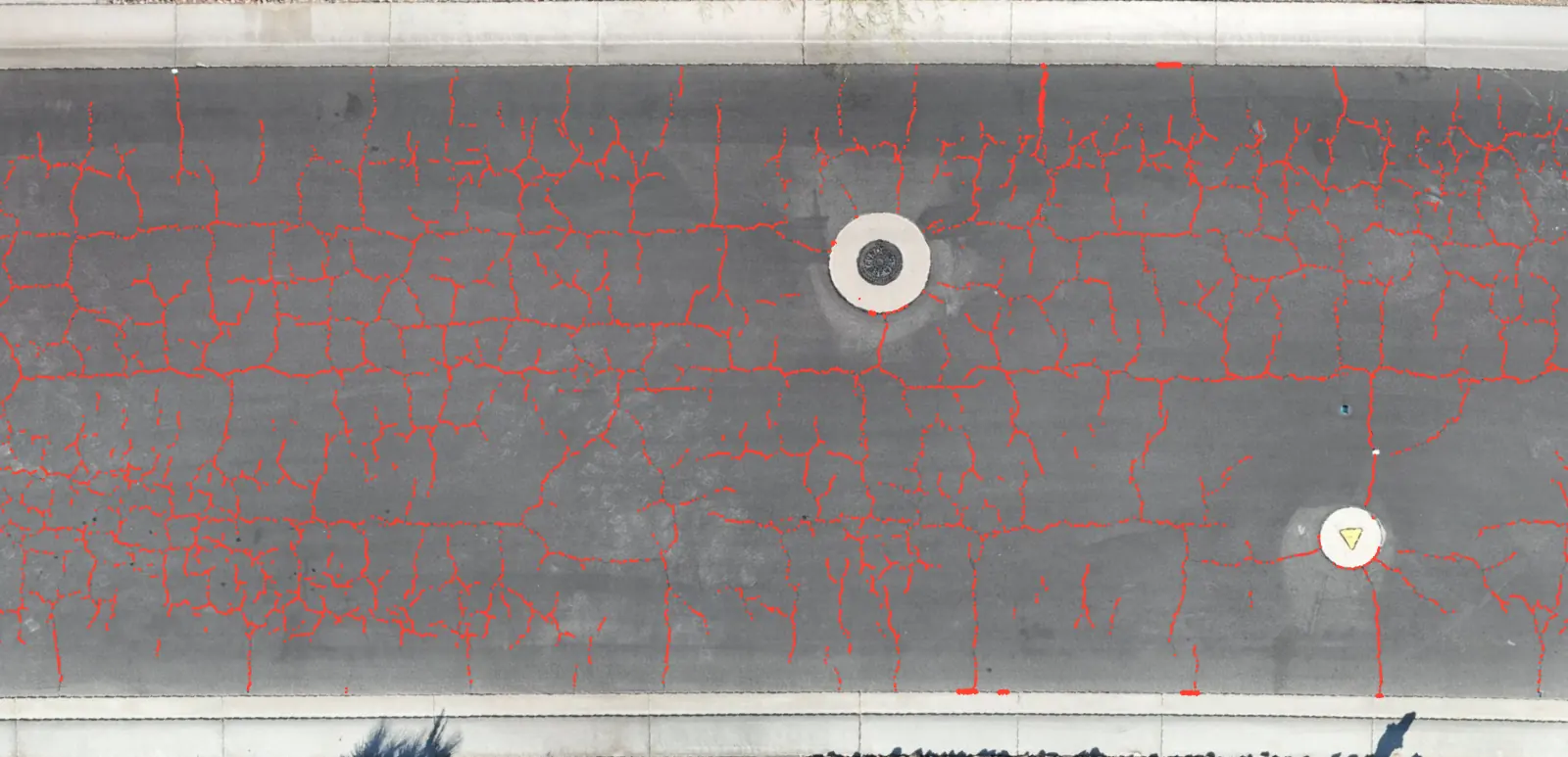 The same top-down road view after HALO AI analysis, every crack traced in bright red lines from curb to curb, down to the hairline cracks around the manhole cover.