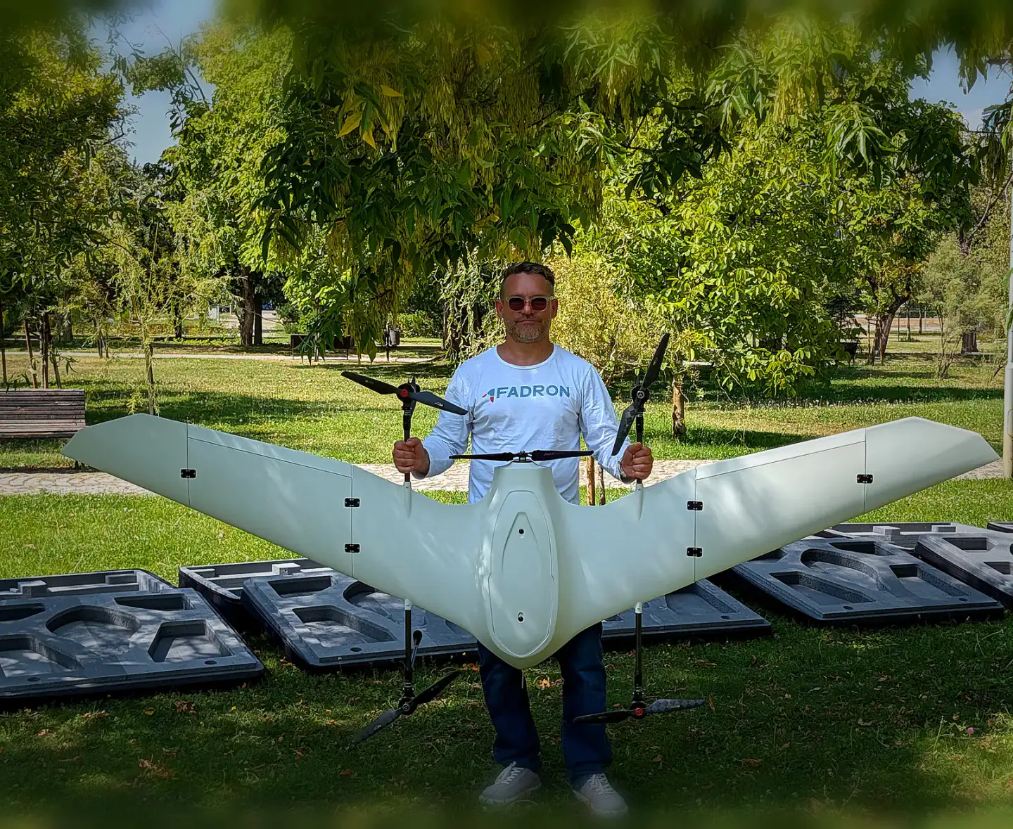 An operator holding a white production Nimbus at full wingspan, open transport cases on the grass behind