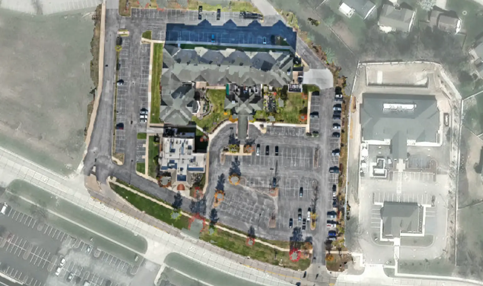 Raw drone image of a parking lot beside an apartment complex, with parked cars, stall lines, and landscaped islands, before HALO AI scores the pavement