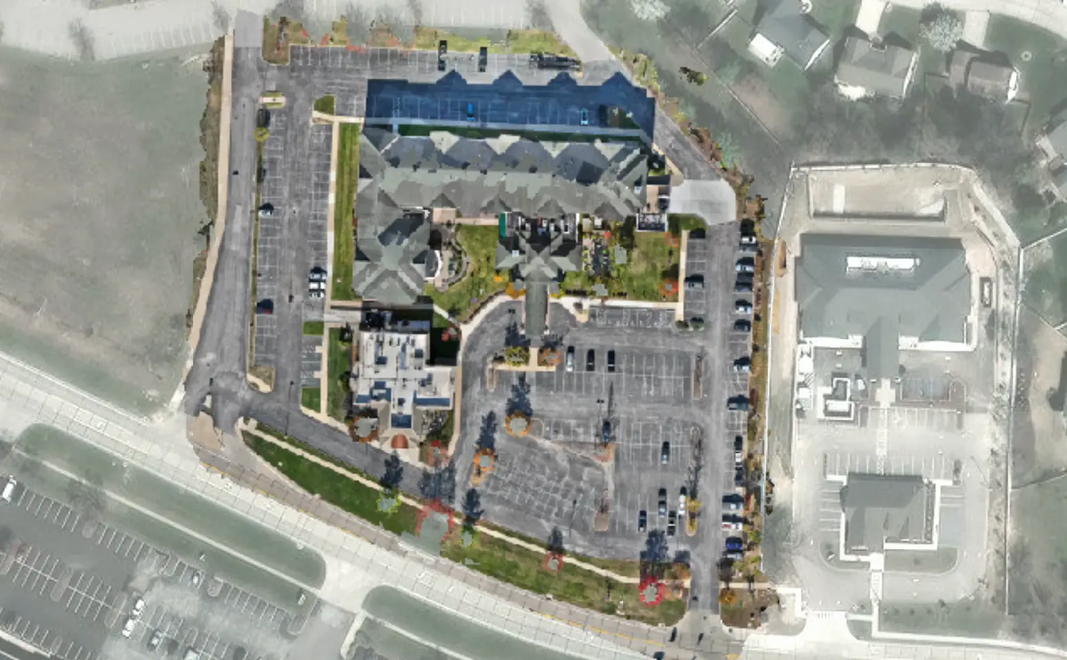 Top-down drone orthomosaic of a parking lot beside an apartment complex, showing stall lines, parked cars, and landscaped islands before any analysis